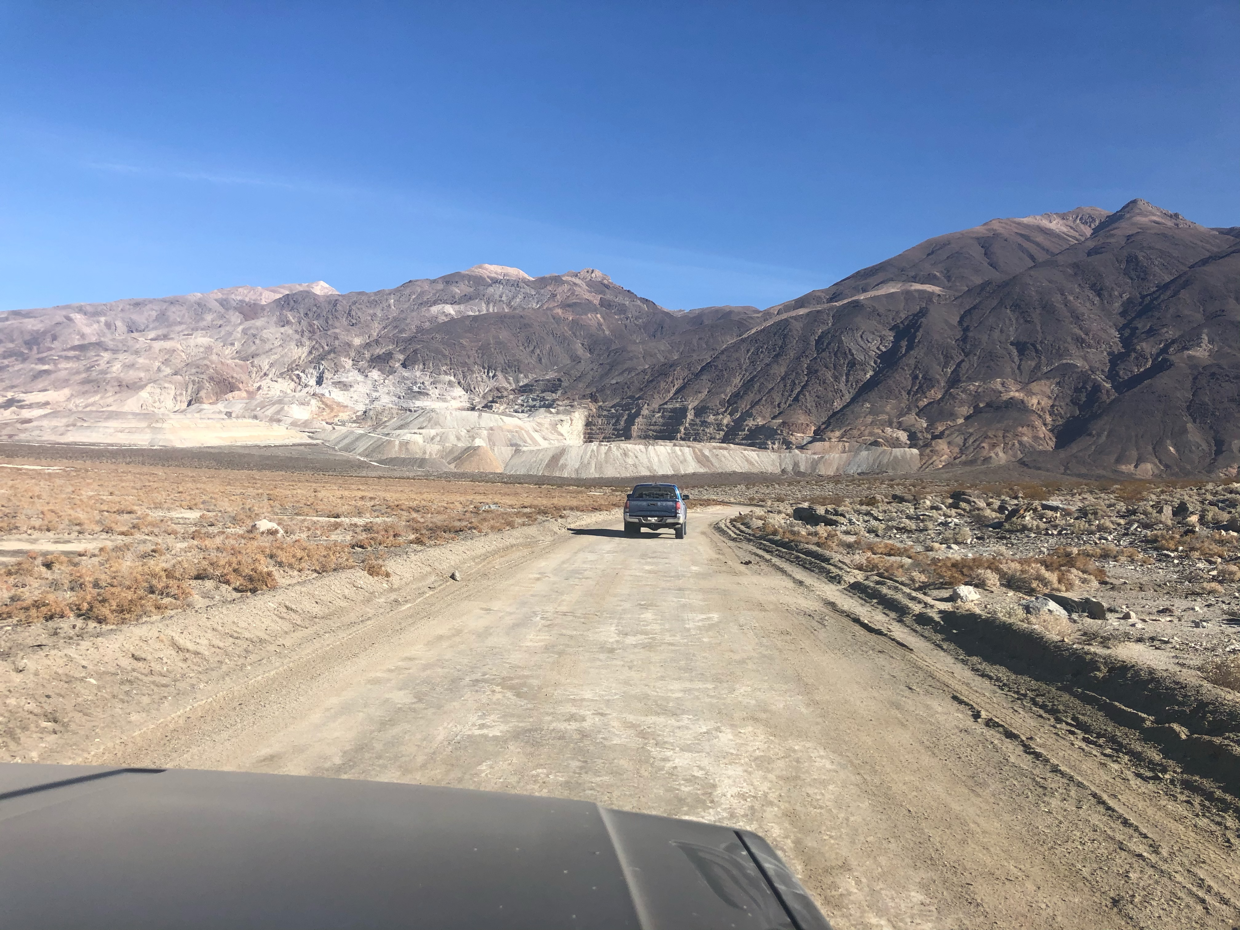 A blue Tacoma on a dirt road with a working mine in the background.
