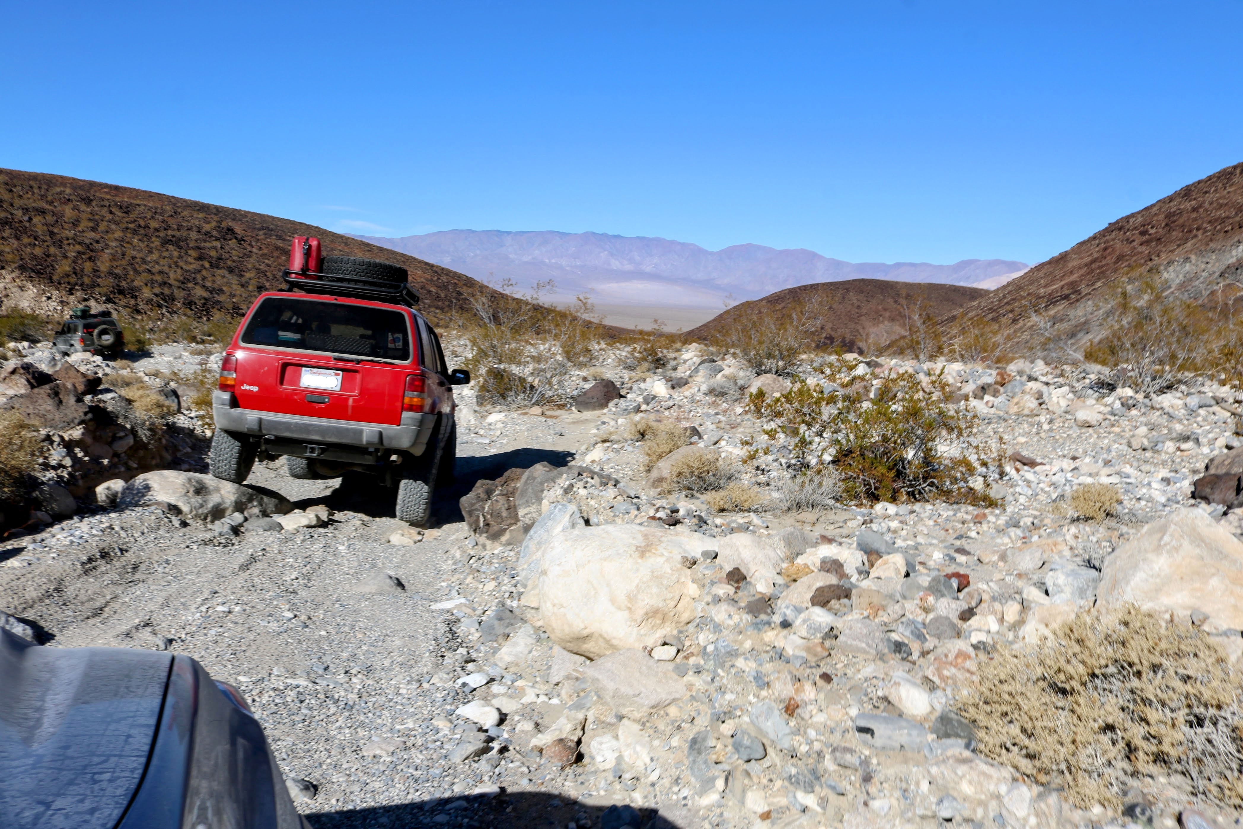 Red Jeep ZJ crawling over rocks on a dirt trail.