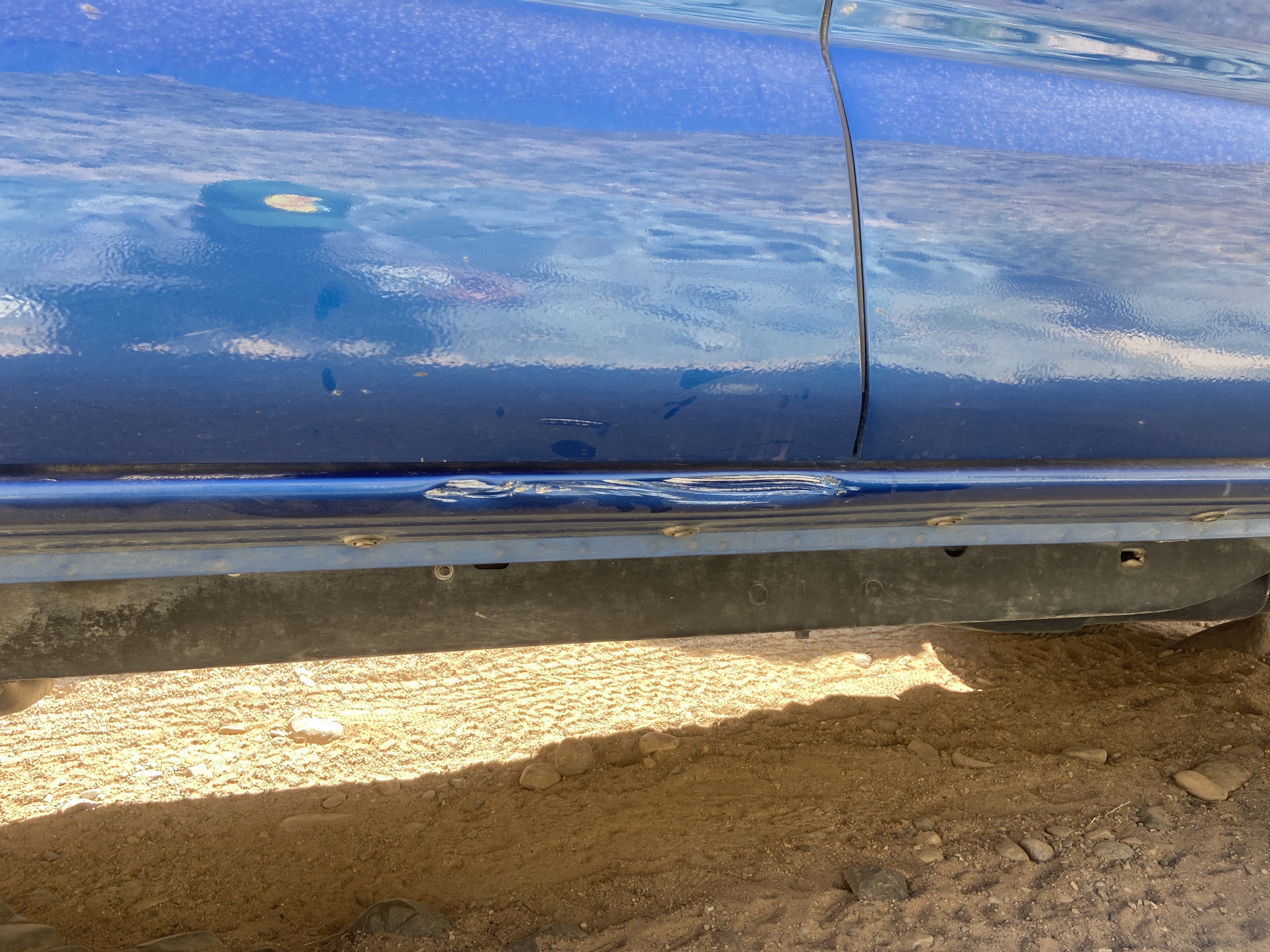 The rocker panel on a blue Tacoma with a dent in it.